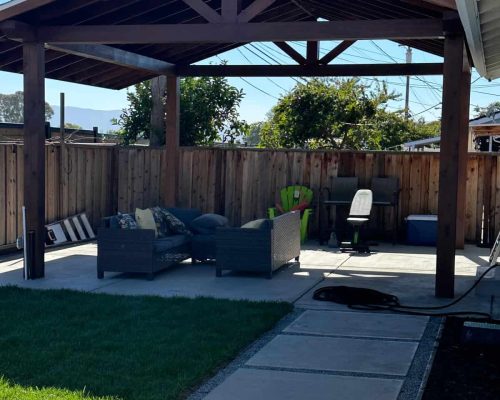 Backyard patio with wooden pergola, outdoor furniture, and green lawn.