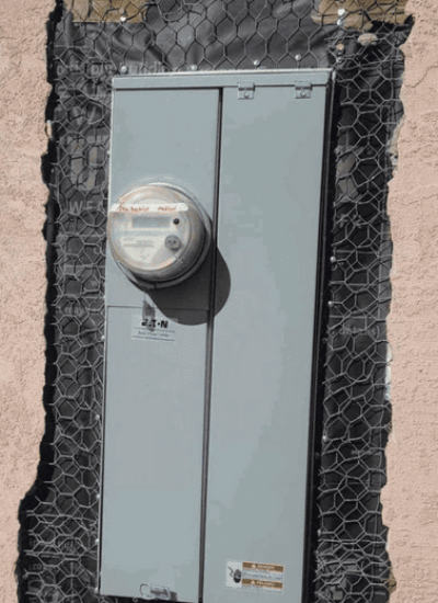 Electrical meter box installed on exterior wall with protective mesh.