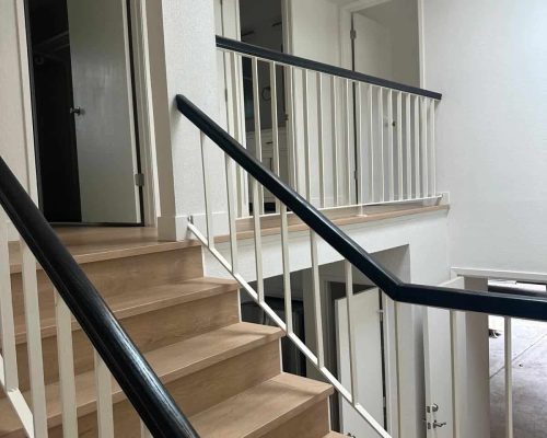 Modern interior staircase with wooden steps and black handrails.
