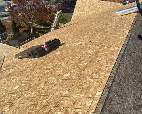 Roof installation in progress with plywood sheathing and tools on the roof.